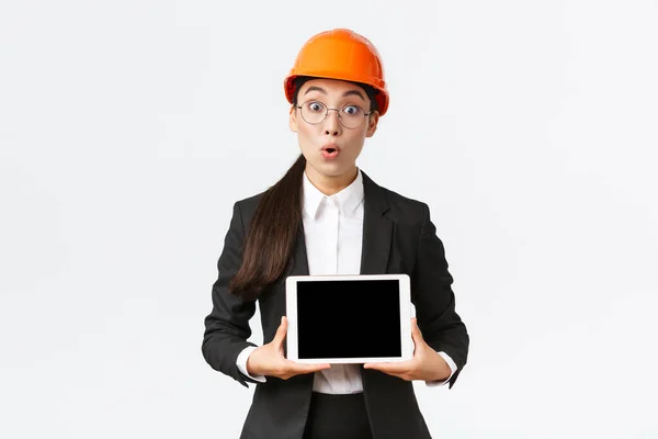Impressionado asiático feminino engenheiro de construção, empresária em capacete de segurança e terno mostrando gráfico, introduzir digrama na tela de tablet digital, de pé espantado sobre fundo branco — Fotografia de Stock