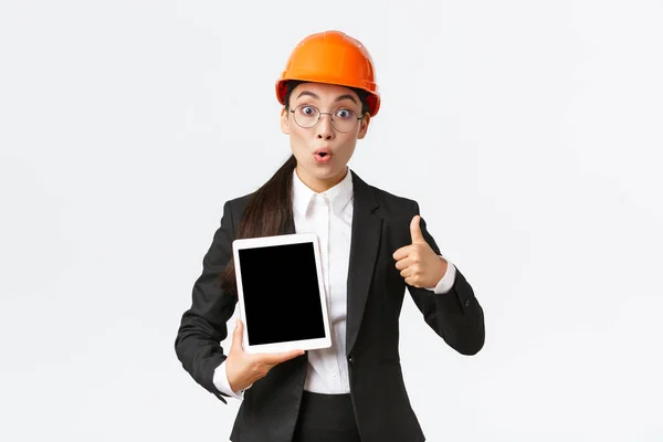 Impressed and excited asian female engineer, industrial technician in business suit and safety helmet showing thumbs-up and digital tablet screen with amazed expression, react to profit diagram — Stock Photo, Image