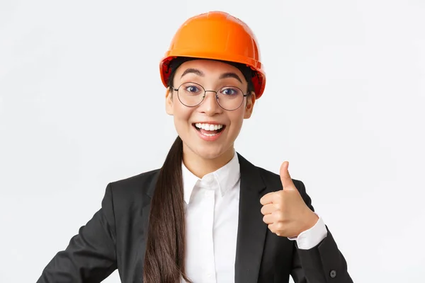 Close-up van professionele tevreden aziatische vrouwelijke chief engineer, architect in business suit en veiligheidshelm tonen duimen-up in goedkeuring, geven toestemming, aanbevelen bouwbedrijf — Stockfoto