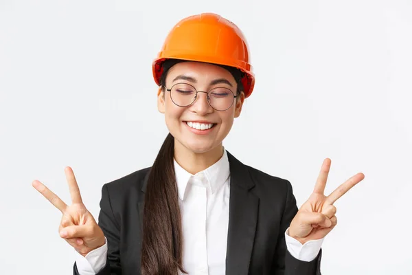 明るい成功した女性アジアのエンジニアのクローズアップ,安全ヘルメットと平和の兆候と笑顔のカワイイを示すビジネススーツの建設建築家,白い背景に立って — ストック写真