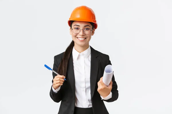 Lächelnde erfolgreiche Unternehmerin, Chefkonstrukteurin in Helm und Anzug, Blaupausen und Stift in der Hand, Vertragsunterzeichnung mit Bauunternehmer, weißer Hintergrund — Stockfoto