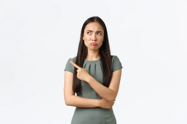 Small business owners, women entrepreneurs concept. Doubtful and skeptical asian businesswoman hesitating, looking uncertain and pouting as pointing finger upper left corner — Stock Photo, Image