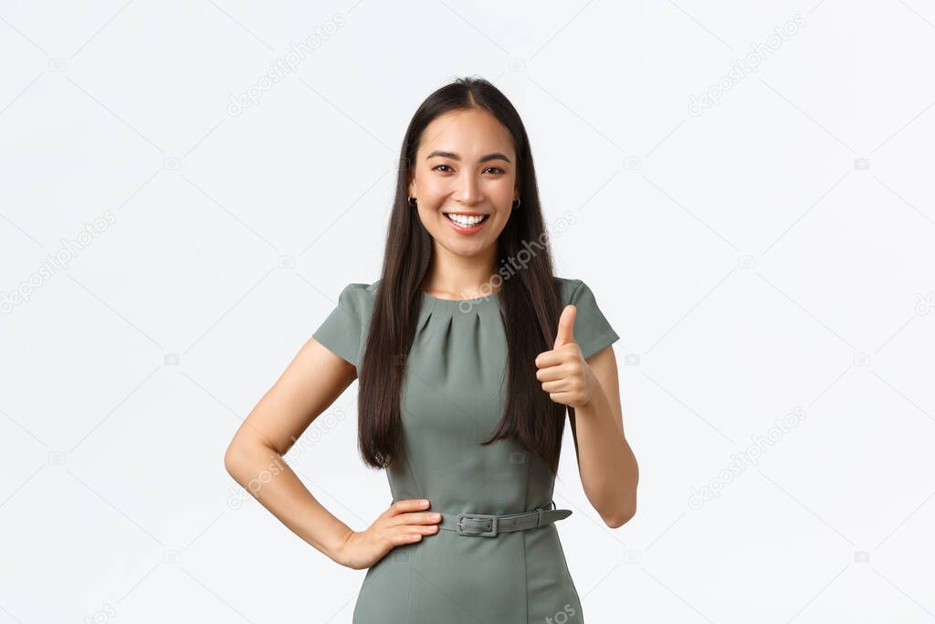 Small business owners, women entrepreneurs concept. Satisfied smiling asian female team leader praising great job, showing thumbs-up in approval, like result, white background