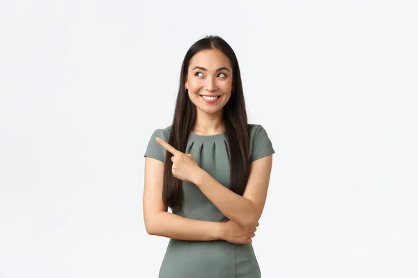 Propietarios de pequeñas empresas, mujeres empresarias concepto. Intrigado feliz asiático hembra en vestido encontrado excelente opción, señalando el dedo a la izquierda y buscando interesado, sonriendo satisfecho, fondo blanco — Foto de Stock