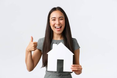 Sigorta, kredi, gayrimenkul ve aile kavramı. Heyecanlı gülümseyen Asyalı kadın, başparmaklarını kaldırıyor ve gülüyor, kağıt evi gösteriyor, apartman dairesi buluyor, broker evini bulmakta yardım ediyor.
