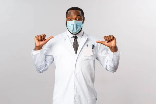 Covid19, healthcare and clinic concept. I am specialist and professional you looking for. Upbeat african-american male doctor pointing at himself and smiling, ask me anything, contact your physician