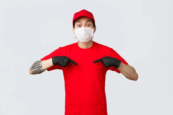 Surpris haletant asiatique livraison homme en bonnet rouge et t-shirt, portant un masque de protection et des gants médicaux pour prévenir la propagation du virus, soins pour la sécurité des clients lors de la livraison auto-qurantine commandes en ligne — Photo