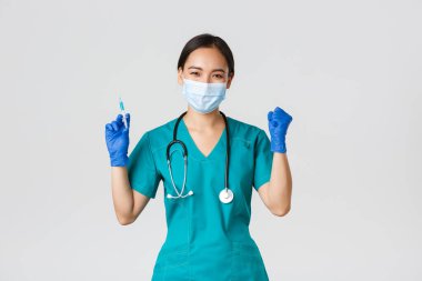 Covid-19, koronavirüs hastalığı, sağlık çalışanları konsepti. Neşeli zafer kazanan Asyalı kadın doktor, tıbbi maske ve eldiven takan doktor, aşıyla şırınga tutarken seviniyor.