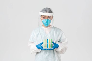 Covid-19, koronavirüs hastalığı, sağlık çalışanları konsepti. Şaşırmış Asyalı kadın doktor, kişisel koruyucu ekipman teknolojisi laboratuarı aşı ya da analizlerle dolu test tüpleri, beyaz arka plan.