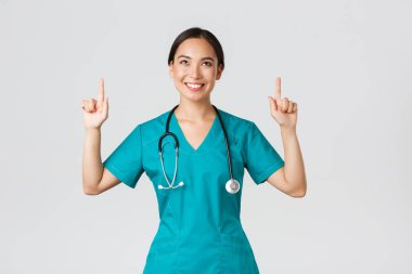 Covid-19, sağlık çalışanları, salgın konsepti. Gülümseyen güzel Asyalı kadın hemşire, önlüklü doktor tatmin olmuş bir sırıtışla yukarı bakıyor, harika bir tanıtım teklifi sunmaktan mutluluk duyuyorum, beyaz arka plan.