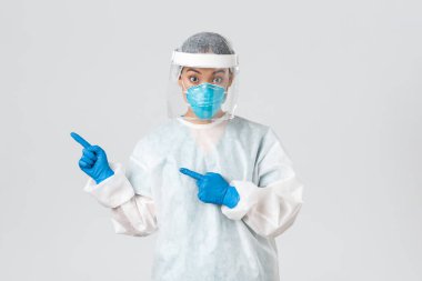 Covid-19, koronavirüs hastalığı, sağlık çalışanları konsepti. Şaşırmış kadın Asyalı doktor, tıbbi solunum cihazı hekimi ve sol üst köşeyi gösteren kişisel koruyucu ekipman.
