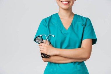 Covid-19, koronavirüs hastalığı, sağlık çalışanları konsepti. Asyalı kadın doktor vücudu gülümsüyor, kollar çapraz göğüste kendinden emin ve steteskop tutuyor, beyaz arka planda duruyor.