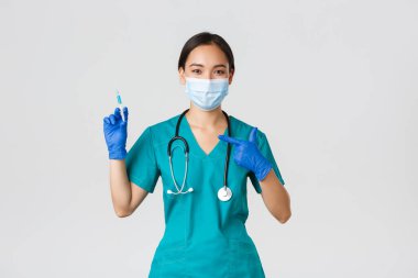 Covid-19, koronavirüs hastalığı, sağlık çalışanları konsepti. Dost canlısı Asyalı kadın doktor, tıbbi maskeli doktor ve şırıngayı aşıyla gösteren önlük.