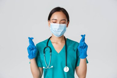 Covid-19, koronavirüs hastalığı, sağlık çalışanları konsepti. Umut verici Asyalı kadın doktor, tıbbi maske ve lastik eldiven giyen doktor, dilek tutuyor, şans diliyor.