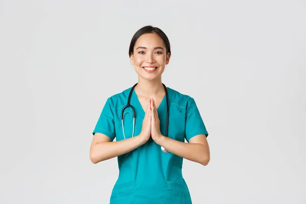 Covid-19, zdravotničtí pracovníci a prevence viru. Usmívající se krásná asijská sestřička, lékař v křoví s úsměvem, držet ruce u sebe přes hruď v namaste, pozdrav gesto — Stock fotografie