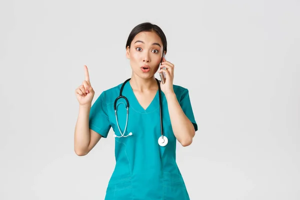 Covid-19, sağlık çalışanları ve virüs konseptini önlemek. Güzel Asyalı kadın doktor portresi, önlüklü hemşire telefonla konuşuyor ve parmak kaldırıyor. — Stok fotoğraf