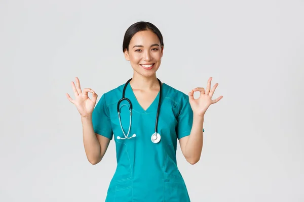 Covid-19, gezondheidswerkers, pandemisch concept. Professionele zelfverzekerde aziatische vrouwelijke arts, stagiaire in scrubs verzekeren patiënten alles goed, tonen oke gebaar tevreden, glimlachen blij — Stockfoto