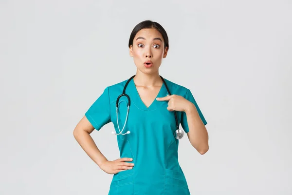 Covid-19, pracownicy służby zdrowia, koncepcja pandemii. Zaskoczony i zaskoczony azjatycki lekarz, pielęgniarka w fartuchu wskazując na siebie, beaing nazwie lub wybrany, stojące białe tło — Zdjęcie stockowe