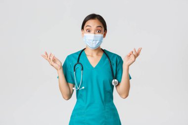 Covid-19, koronavirüs hastalığı, sağlık çalışanları konsepti. Şaşırmış ve şaşırmış Asyalı kadın hemşire, tıbbi maskeli doktor ve önlüklü doktor heyecanlı bir şekilde ellerini kaldırıyor, inanılmaz haberler duyuyor, beyaz arka plan