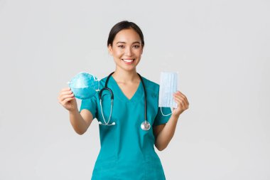 Covid-19, koronavirüs hastalığı, sağlık çalışanları konsepti. Ameliyat maskesi takan neşeli, gülümseyen Asyalı kadın doktor ama solunum cihazını hastaya vermeyi öneriyor.