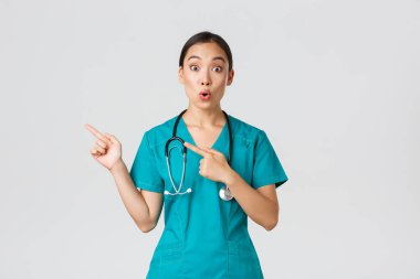 Covid-19, sağlık çalışanları, salgın konsepti. Önlüklü Asyalı kadın hemşire merak uyandıran bir ifadeyle soru soruyor. Doktor heyecanlı görünüyor ve sol üst köşeyi işaret ediyor.