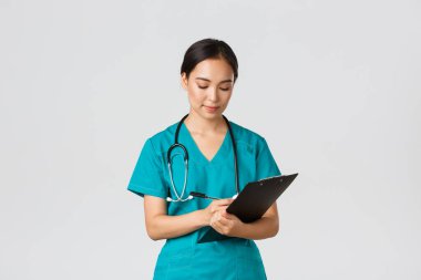 Sağlık çalışanları, virüsü önleme, karantina kampanyası konsepti. Ciddi görünümlü kadın doktor, önlüklü hemşire. Dosyaya bilgi yazıyor, hastayı muayene ediyor, beyaz bir geçmişi var.