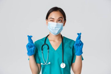 Covid-19, koronavirüs hastalığı, sağlık çalışanları konsepti. Umut dolu Asyalı doktor. Maskeli ve eldivenli. Sol üst köşeye bakıyor ve dua ediyor.