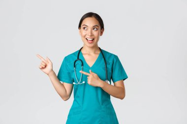 Covid-19, sağlık çalışanları, salgın konsepti. Neşeli gülümseyen Asyalı kadın hemşire, önlüklü doktor, sol üst köşeye bakıyor ve işaret ediyor.