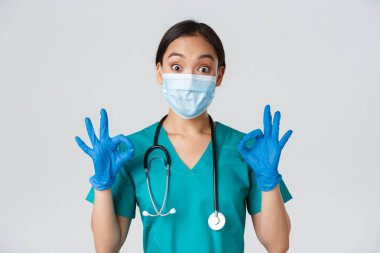 Covid-19, koronavirüs hastalığı, sağlık çalışanları konsepti. Heyecanlı ve etkilenmiş Asyalı doktor, tıbbi maskeli hemşire ve lastik eldiven iyi bir hareket, onay ya da övgü gösteriyor.