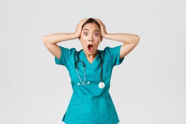 Covid-19, sağlık çalışanları ve virüs konseptini önlemek. Şok olmuş ve endişeli Asyalı kadın doktor, paniklemiş, kafasını tutup çığlık atıyor, büyük bir sorun yaşıyor, başı belada, beyaz arka plan