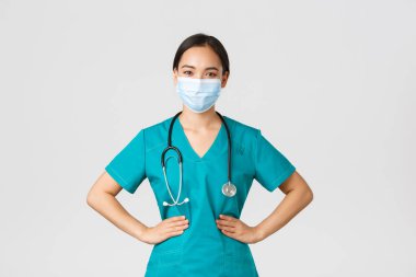 Covid-19, koronavirüs hastalığı, sağlık çalışanları konsepti. Kendine güvenen profesyonel doktor, tıbbi maskeli doktor ve vardiya kliniğinde çalışan önlüklü. Kararlı, beyaz bir geçmişi var.