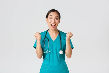 Covid-19, sağlık çalışanları ve virüs konseptini önlemek. Umut dolu ve rahatlamış, neşeli Asyalı güzel kadın doktor yumruklarla sevinen doktor, tebrik ya da övgü dolu biri, kazanan.