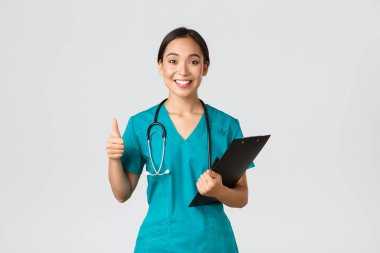 Sağlık çalışanları, virüsü önleme, karantina kampanyası konsepti. Gülümseyen güzel Asyalı doktor, önlüklü kadın stajyer, başparmağını kaldır, not panosunu tut, olumlu sonuçlar getir, beyaz arka plan