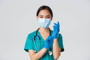 Covid-19, koronavirüs hastalığı, sağlık çalışanları konsepti. Profesyonel gülümseyen Asyalı kadın doktor, tıbbi maske ve önlüklü doktor, lastik eldiven giyin ro muayene, beyaz arka plan