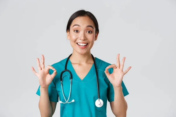 Trabalhadores de saúde, prevenção de vírus, conceito de campanha de quarentena. excitado e satisfeito asiático feminino médico, enfermeira em esfoliação com estetoscópio, mostrando ok gesto, fundo branco — Fotografia de Stock