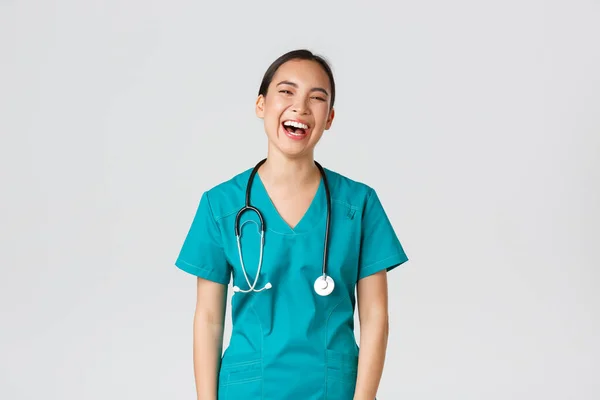 Covid-19, εργαζόμενοι στην υγειονομική περίθαλψη, πανδημία έννοια. Ξέγνοιαστη όμορφη Ασιάτισσα νοσοκόμα με ποδιά, ειδικευόμενη που διασκεδάζει, γελώντας χαρούμενη. Ο γιατρός στο διάλειμμα γέλασε και μίλησε με συναδέλφους. — Φωτογραφία Αρχείου