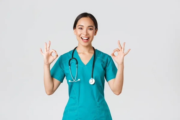 Covid-19, egészségügyi dolgozók, világjárvány. Szakmai magabiztos ázsiai női orvos, gyakornok köpenyben biztosítja a betegek minden jót, mutatja rendben gesztus elégedett, mosolygós elégedett — Stock Fotó