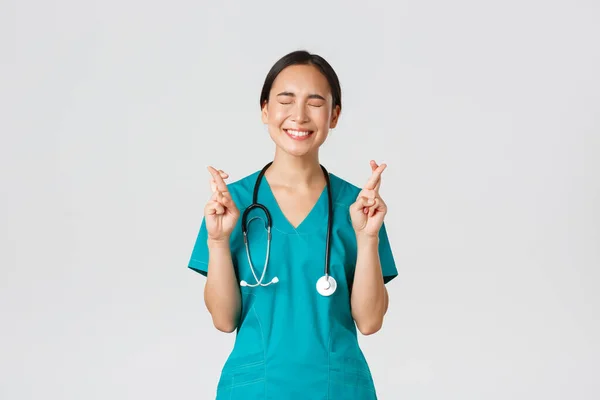 Covid-19, profissionais de saúde, conceito pandémico. Otimista feliz e esperançoso asiático enfermeira feminina, estagiária à espera de promoção, cruz dedos boa sorte e fechar os olhos, sorrindo animado — Fotografia de Stock
