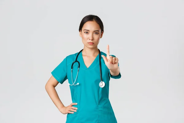 Covid-19, pracownicy służby zdrowia, koncepcja pandemii. Poważny wygląd profesjonalny kobieta azjatycki lekarz w fartuch, lekarz potrząsający palec w prohibicji, ostrzegawczy gest, zakazać coś — Zdjęcie stockowe