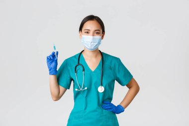 Covid-19, koronavirüs hastalığı, sağlık çalışanları konsepti. Kendine güvenen Asyalı kadın hemşire, tıbbi maskeli doktor ve lastik eldivenli, aşılı şırınga tutan, beyaz arka planda duran