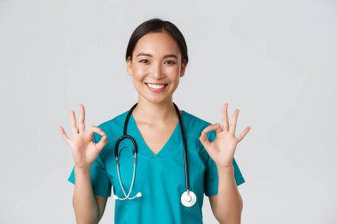 Sağlık çalışanları, virüsü önleme, karantina kampanyası konsepti. Tatmin olmuş yakışıklı Asyalı hemşire, doktor onaylı jest gösteriyor, mükemmel hizmeti öneriyor ya da garanti ediyor.