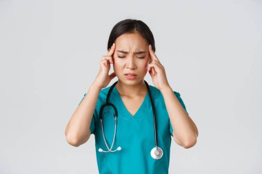 Sağlık çalışanları, virüsü önleme, karantina kampanyası konsepti. Aşırı çalışan ve yorgun Asyalı doktorların yakın plan fotoğrafları, baş ağrısı çeken, sorunlu görünen, ayakta duran beyaz arka plan