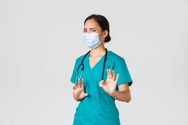 Covid-19, coronavirus disease, healthcare workers concept. Displeased asian female doctor, physician or nurse avoiding contact with germs, wear medical mask and scrubs, shaking hands refusal