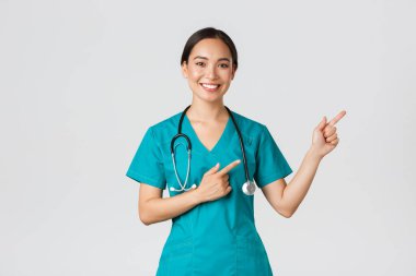 Covid-19, sağlık çalışanları, salgın konsepti. Gülümseyen güzel Asyalı kadın hemşire, sağ üst köşeyi gösteren stajyer doktor, check-up için davetiye, online klinik randevusu, beyaz arka plan