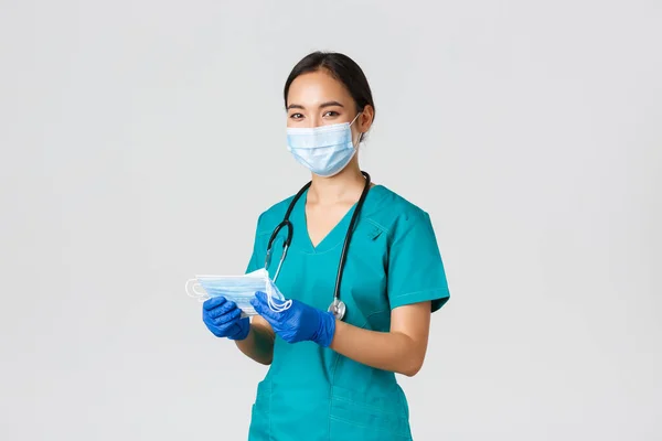 Covid-19, koronavirüs hastalığı, sağlık çalışanları konsepti. Gülümseyen dost canlısı bayan hemşire, önlüklü doktor ve lastik eldiven hastalara tıbbi maske, beyaz arka plan sağlıyor. — Stok fotoğraf
