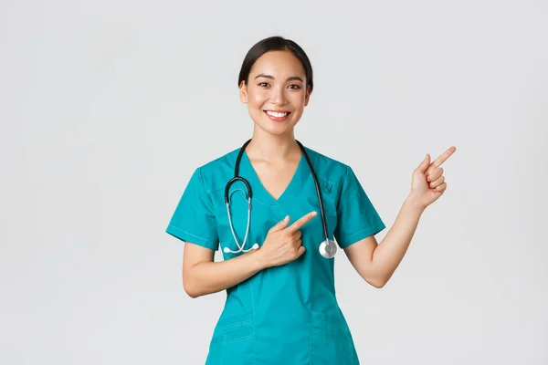 Covid-19 、医療従事者、パンデミックの概念。笑顔美しいアジアの女性看護師,インターン指差指右上隅,検査のための招待,オンラインクリニックの予約,白い背景 — ストック写真