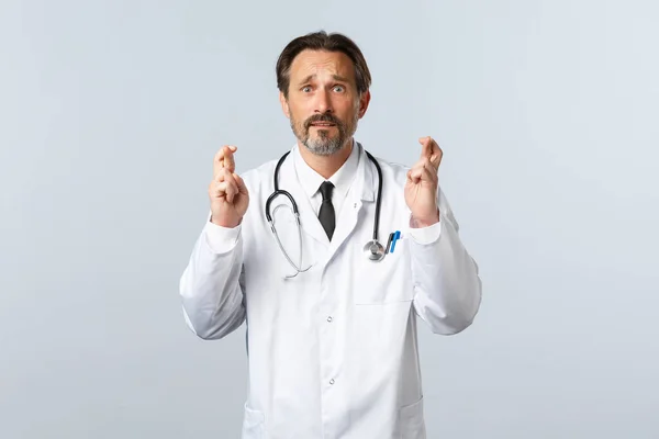 Covid-19, coronavirus outbreak, healthcare workers and pandemic concept. Hopeful anxious male doctor pleading desperate, cross fingers good luck, making wish as feeling worried — Stock Photo, Image