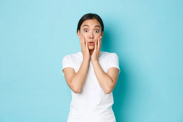 Surpris et étonné asiatique femme étudiante réagir à des nouvelles étonnantes, regardant impressionné, haletant et disant wow impressionné, debout fond bleu clair étonné — Photo