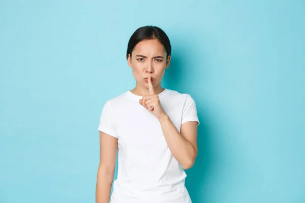 Lifestyle, beauty and shopping concept. Angry and bothered, annoyed asian girl tell to shut up, quiet please, shushing with mad pissed-off face, bossy look, standing blue background — Foto de Stock