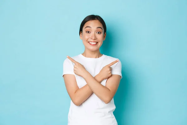 Весела, щаслива і збуджена азіатська дівчина в білій футболці, спрямовуючи пальці вбік, показуючи ліві і правильні варіанти, демонструвати вибір для вас, посміхаючись б'ється над синім тлом — стокове фото